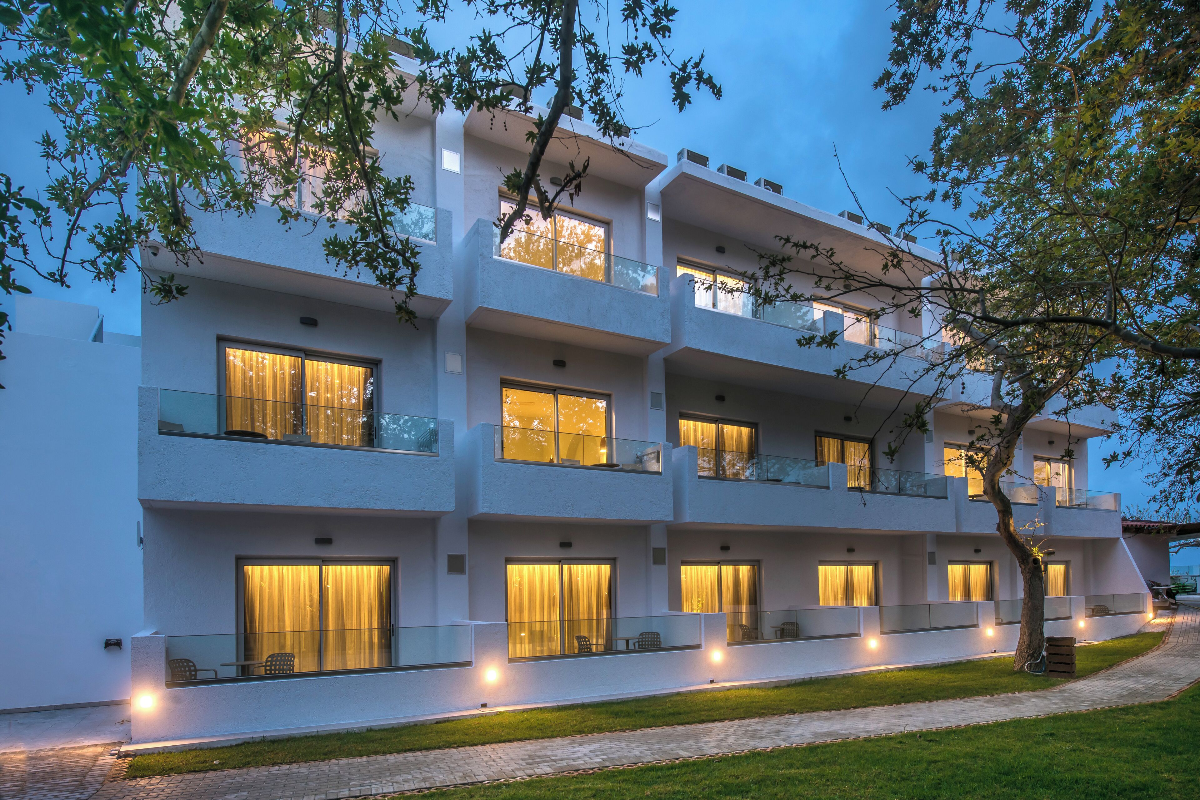 A multi-story hotel with balconies, large windows, and a paved pathway.