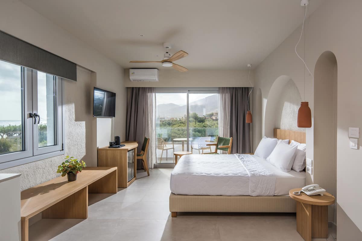 Een moderne hotelkamer met een groot bed, een bureau, een stoel, een klein tafeltje en een balkon met uitzicht op de bergen.