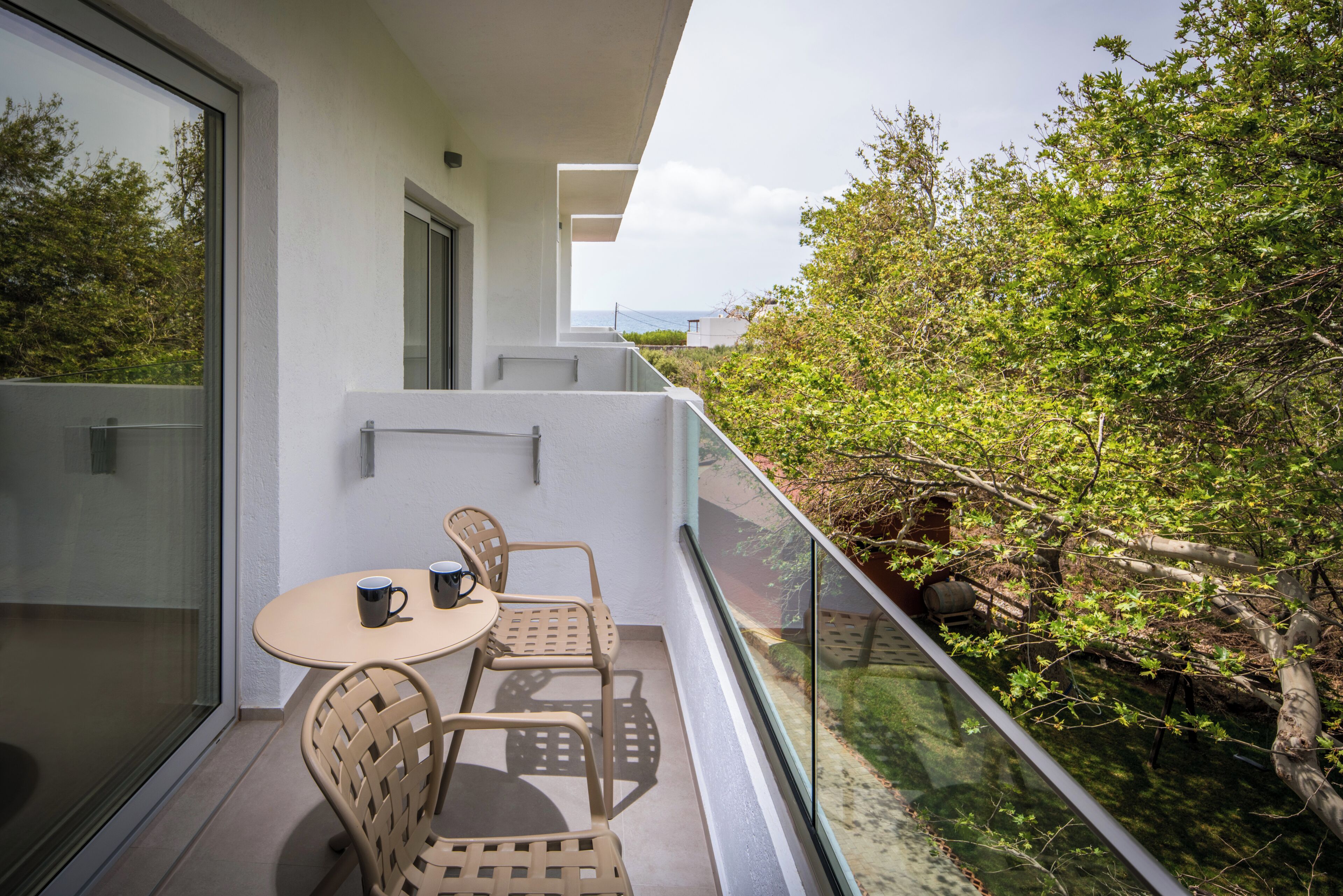 Un balcon avec une table et des chaises, une rambarde en verre et une vue sur la verdure.