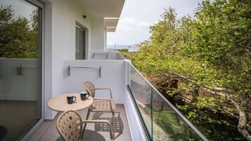 Un balcon avec une table et des chaises, une rambarde en verre et une vue sur la verdure.