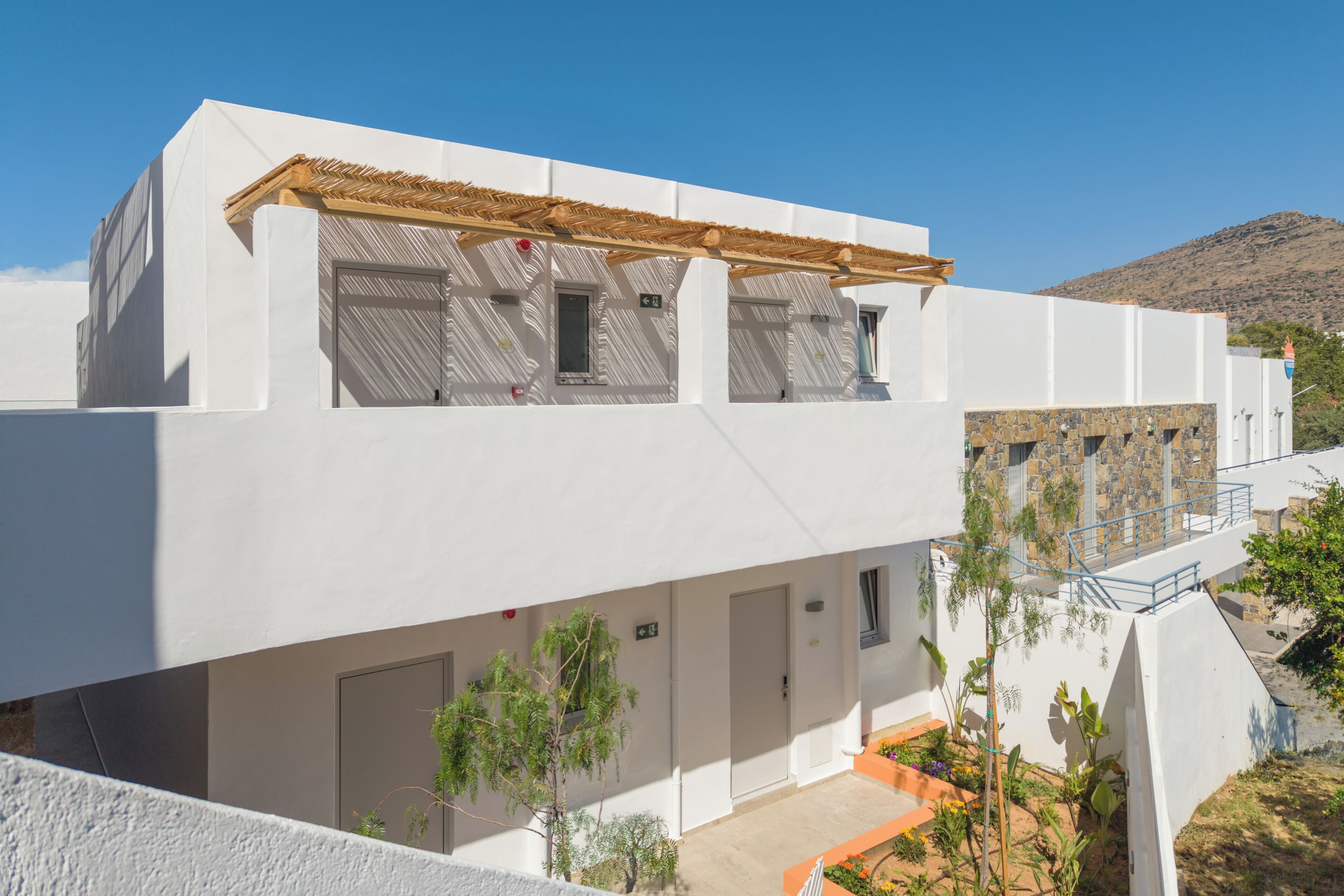 A white building with a wooden pergola, a stone wall, and a staircase leading to a balcony.