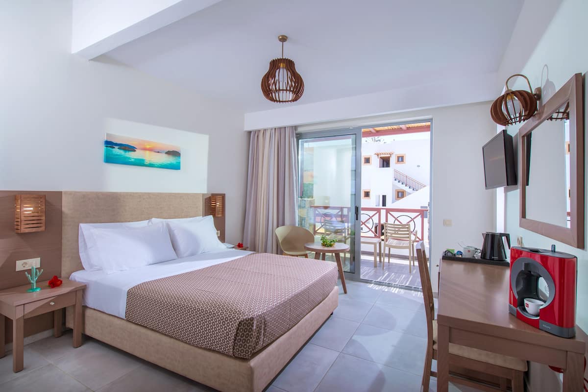 Een hotelkamer met een bed, een bureau, een stoel, een televisie en een balkon met uitzicht.