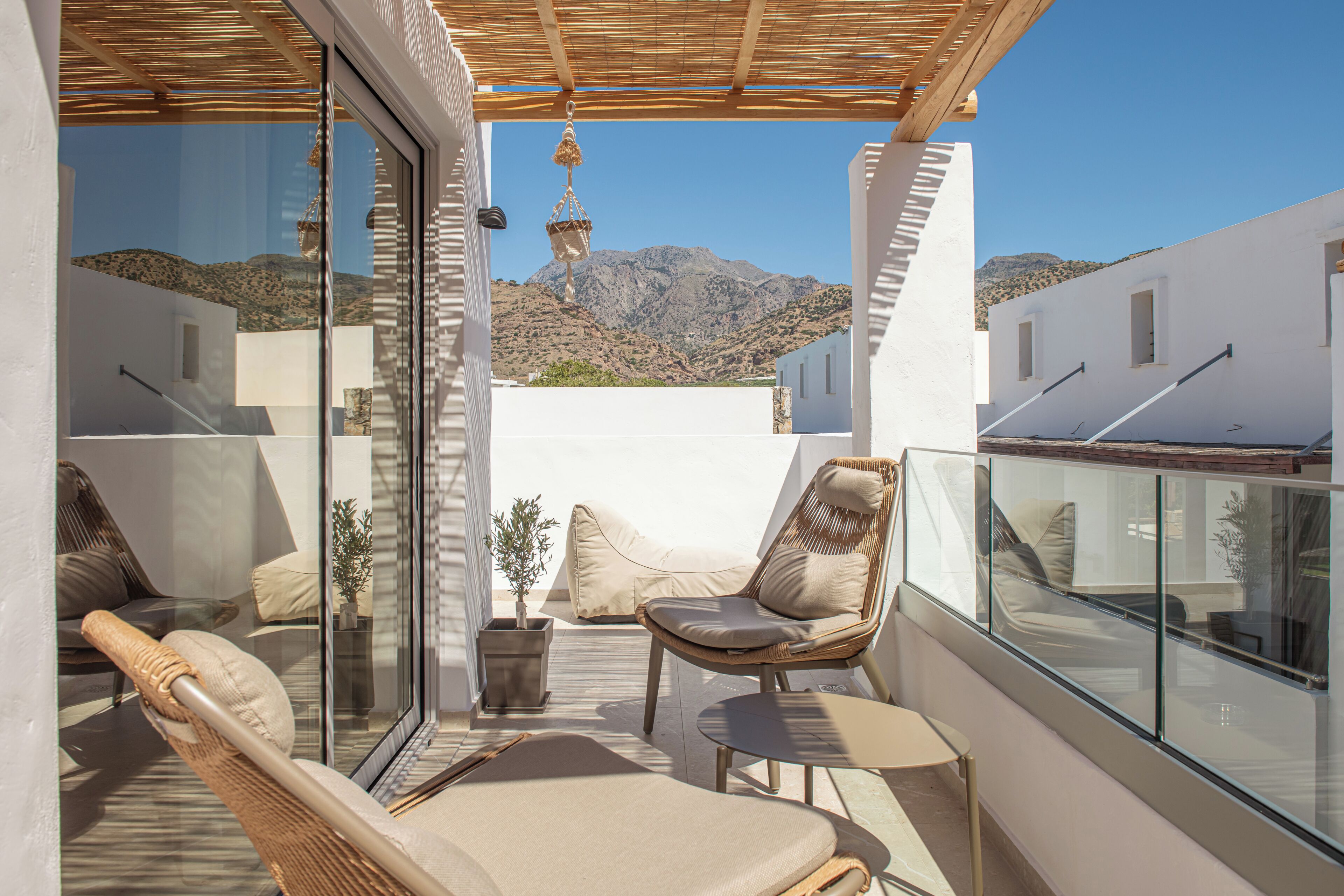 Un balcón con mobiliario de mimbre, una planta en maceta y vistas a un paisaje montañoso.