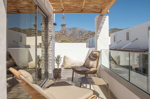 Un balcón con mobiliario de mimbre, una planta en maceta y vistas a un paisaje montañoso.