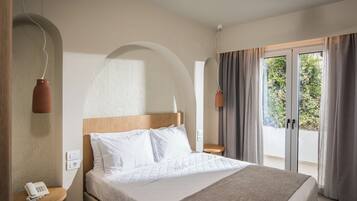 A hotel room with a bed, a bedside table with a phone, a window with curtains, and a view of greenery outside.