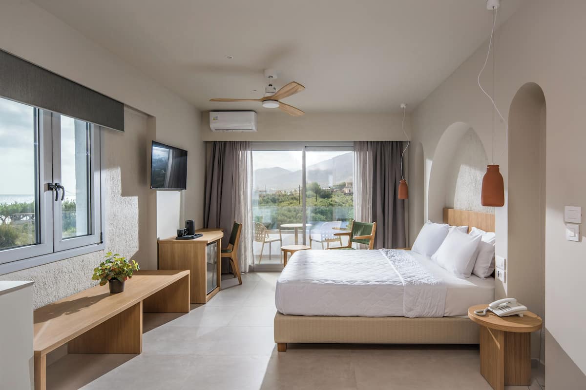 Een moderne hotelkamer met een groot bed, een bureau, een stoel, een klein tafeltje en een balkon met uitzicht op de bergen.