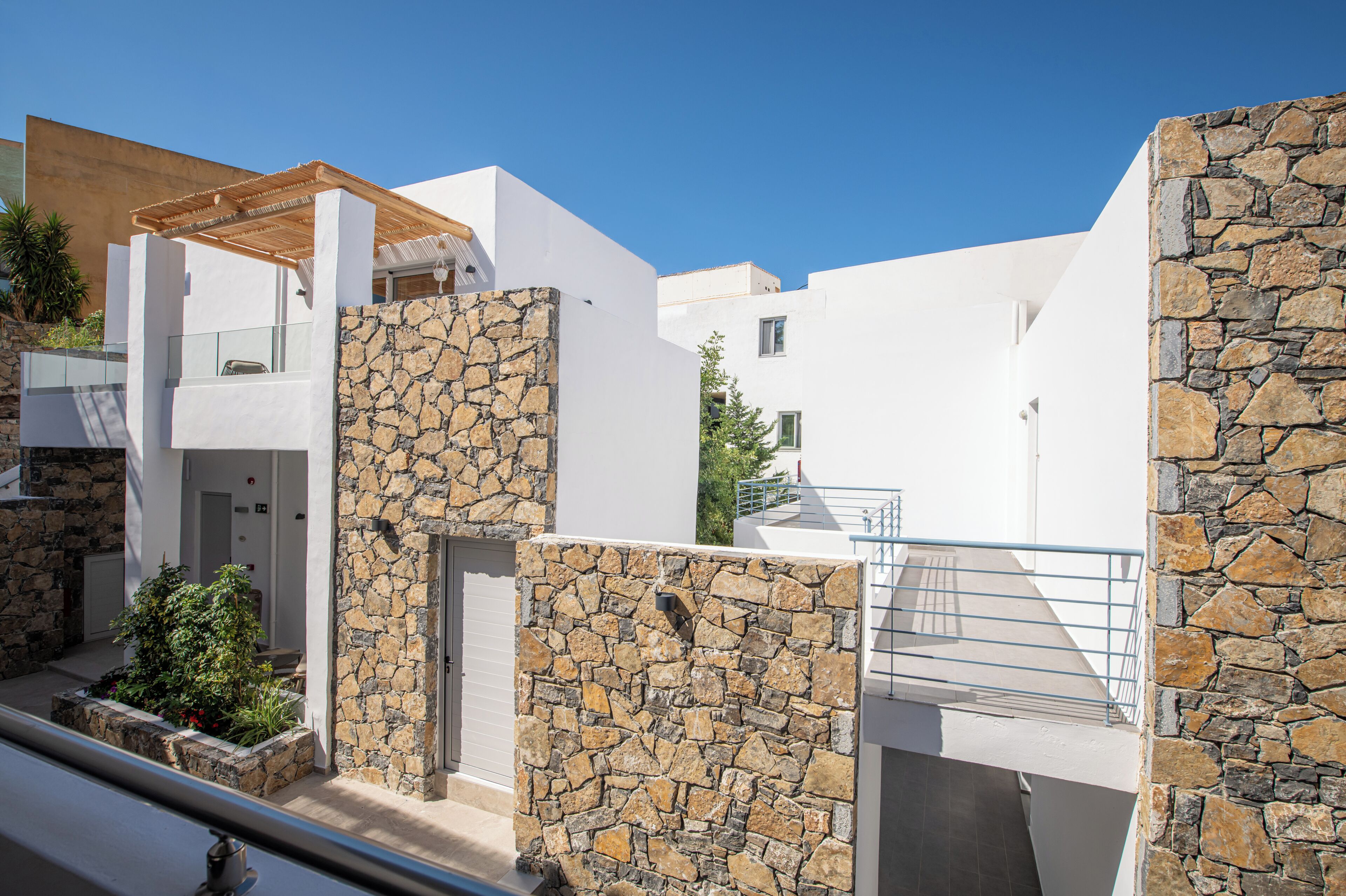 En moderne bygning med stenvægge, en træpergola og en balkon med gelænder.