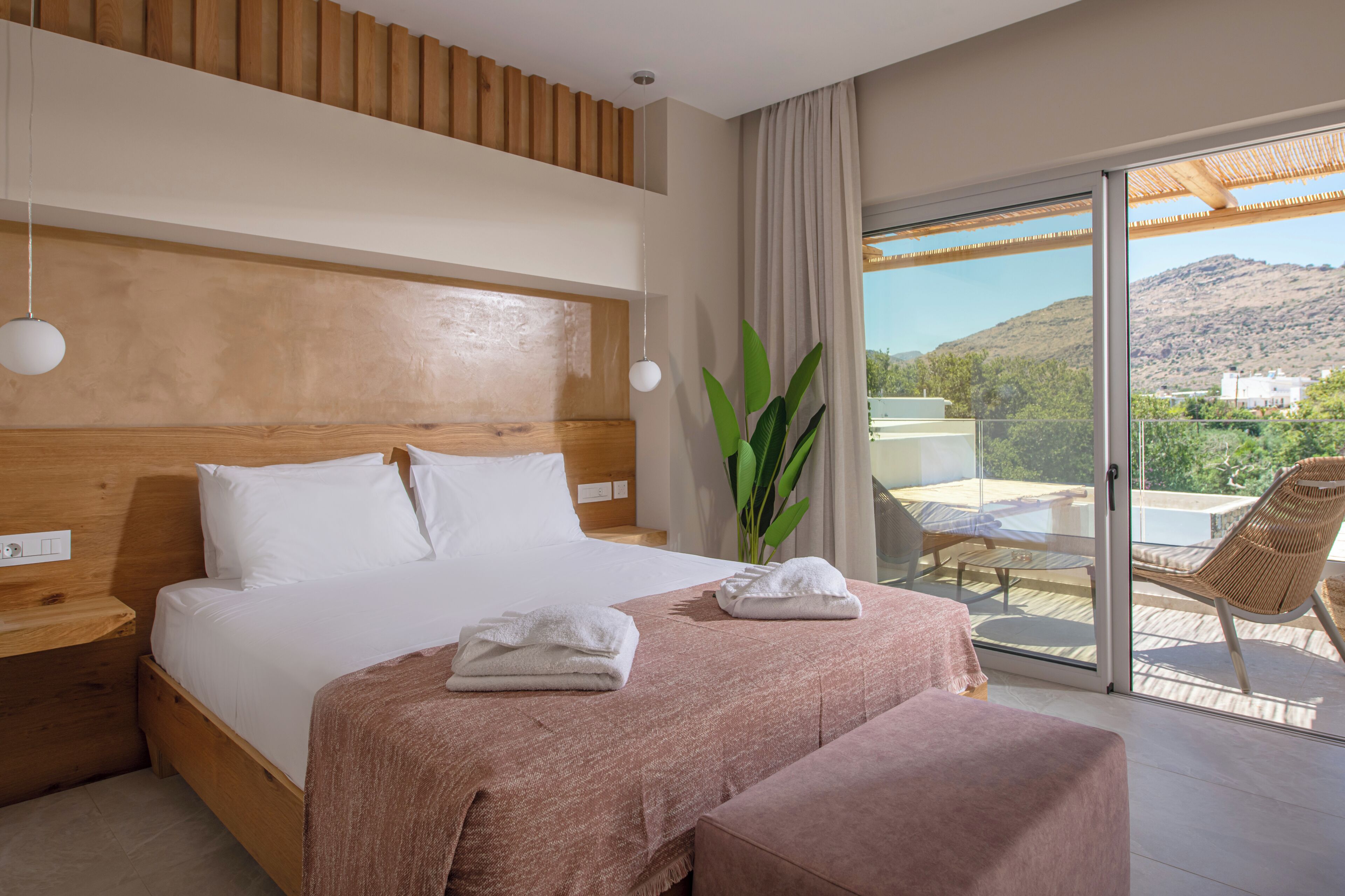 Una habitación de hotel con una cama, una mesita de noche, una planta y un balcón con una silla y una mesa.