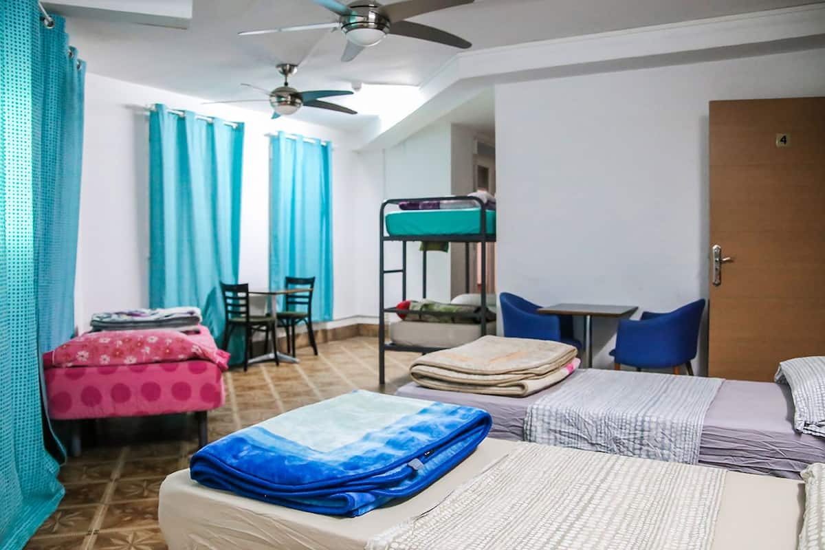 A dormitory room with bunk beds, a desk, chairs, and a ceiling fan.