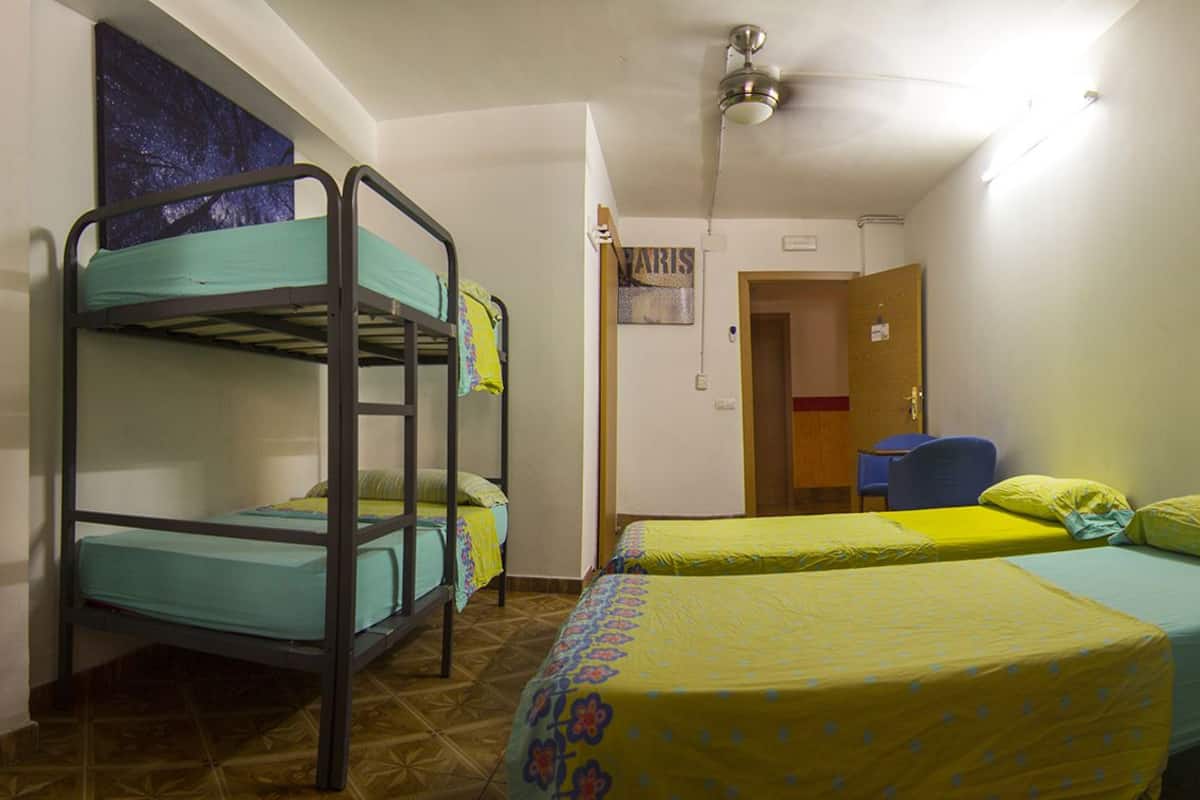 A dormitory room with bunk beds, a desk, and a chair.