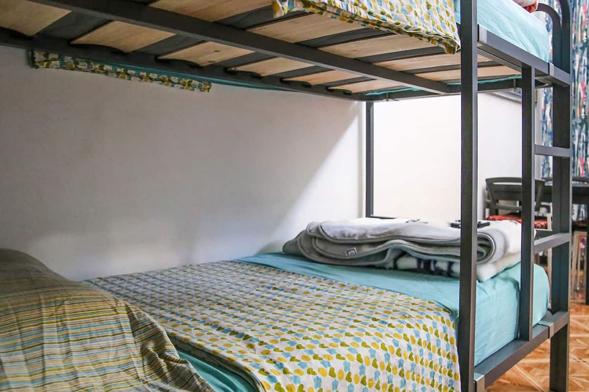 A bunk bed room with a patterned bedspread, a neatly folded blanket, and a small table with a chair.