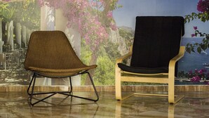 Two chairs with different back designs, one with a woven seat and the other with a solid back, placed on a tiled floor with a view of a coastal landscape through a window. - Go BCN Hi Sants - Hostel (Barcelona)