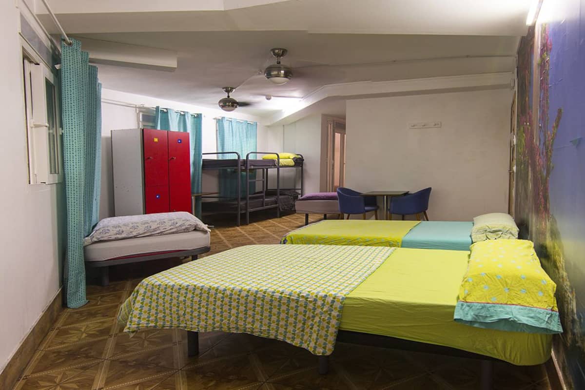 A dormitory room with bunk beds, a desk, chairs, and a ceiling fan.