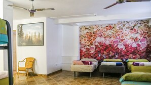 A room with a ceiling fan, a bed with a floral wall mural, a chair, and a bed with a green bedspread. - Go BCN Hi Sants - Hostel (Barcelona)