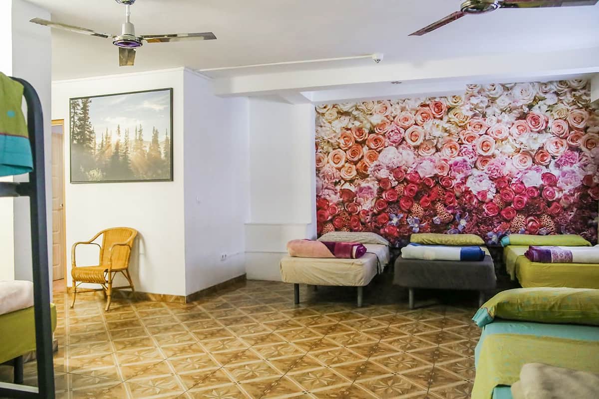A room with a ceiling fan, a bed with a floral wall mural, a chair, and a bed with a green bedspread.