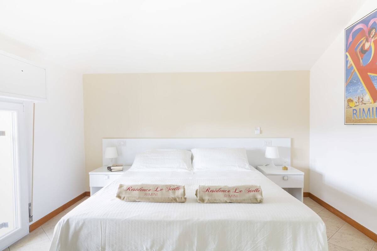 A hotel room with a large bed, two bedside tables, and a window.