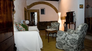 A cozy living room with a white sofa, patterned armchairs, a wooden coffee table, and a lamp. An arched doorway leads to another room. - Palazzo Contino (Bagnoregio)