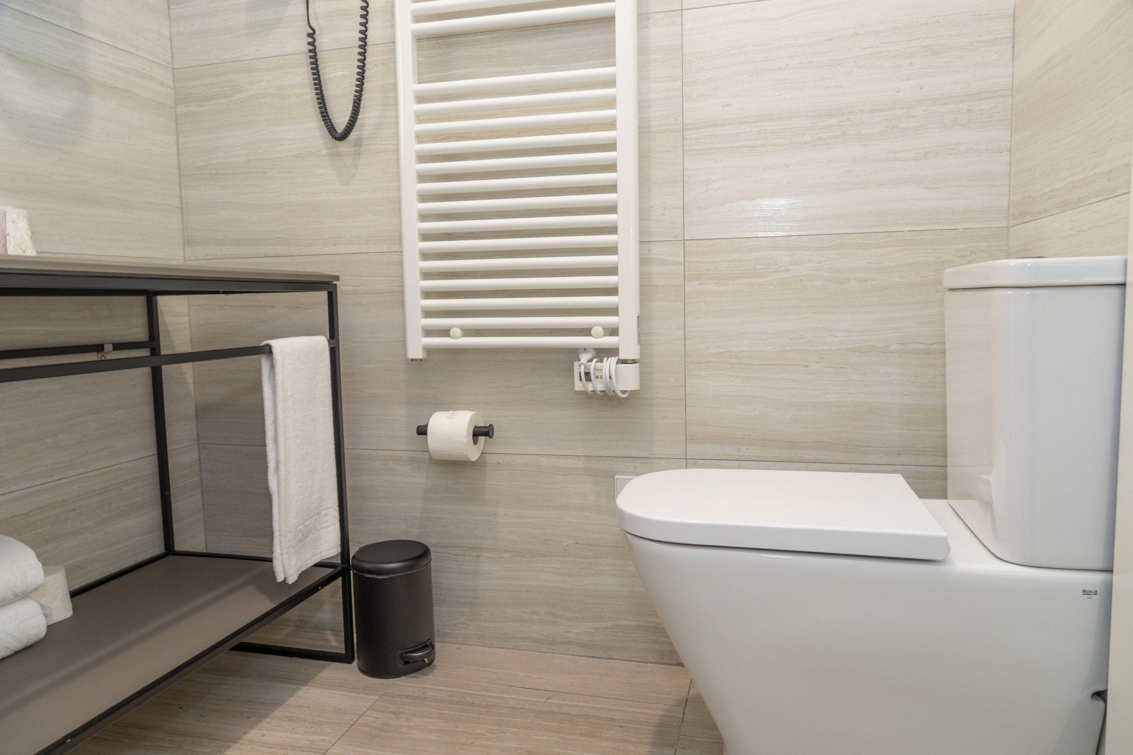 A modern bathroom with a toilet, a towel rack, a trash bin, and a towel on a shelf.