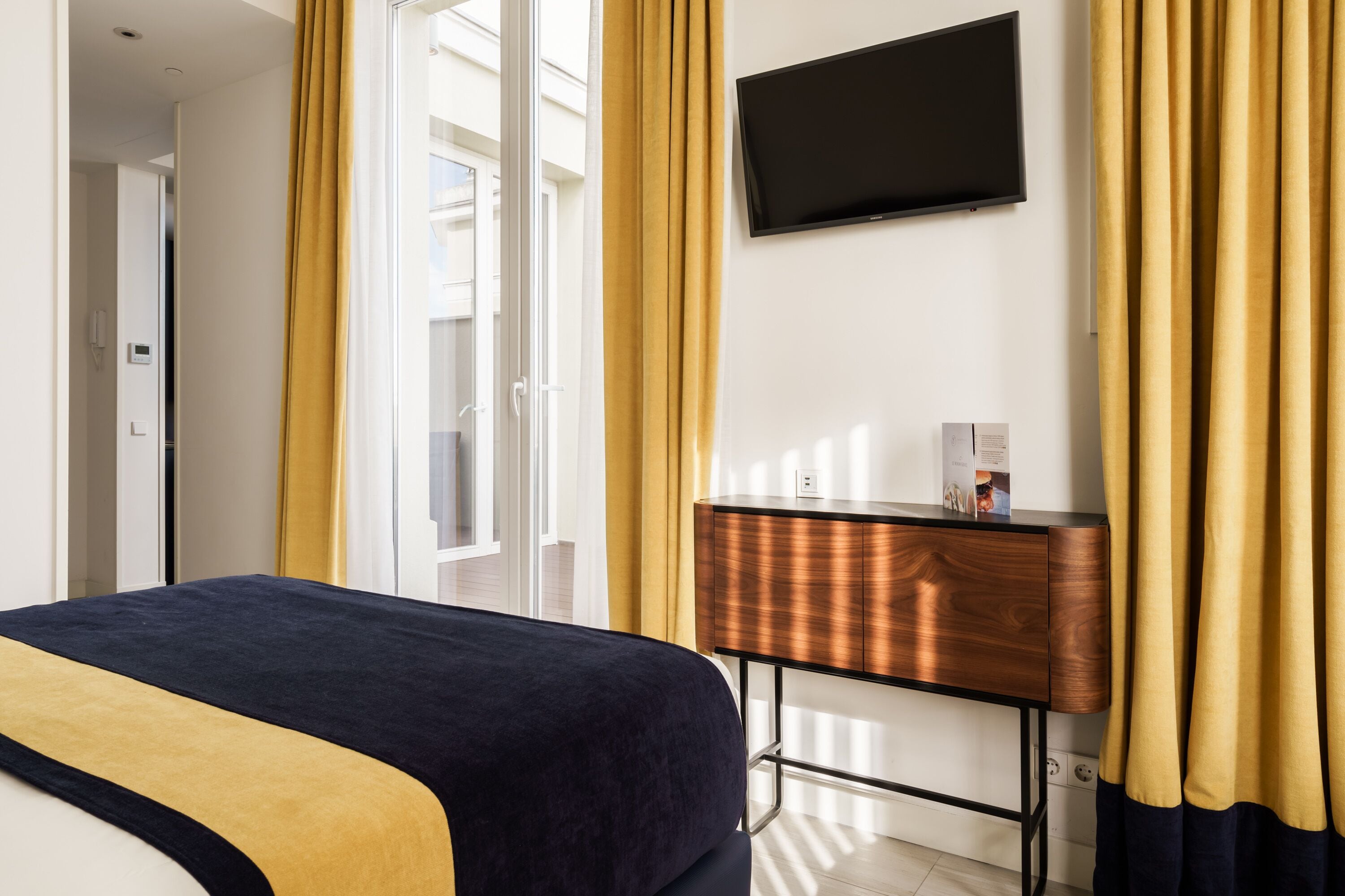 Habitación de hotel con cama, mesita de noche de madera, televisor de pantalla plana y puerta corrediza de vidrio al exterior.