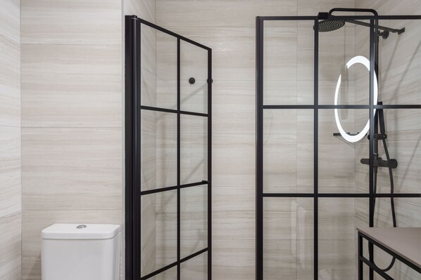 Un baño moderno con cabina de ducha de vidrio, inodoro y tocador con espejo.
