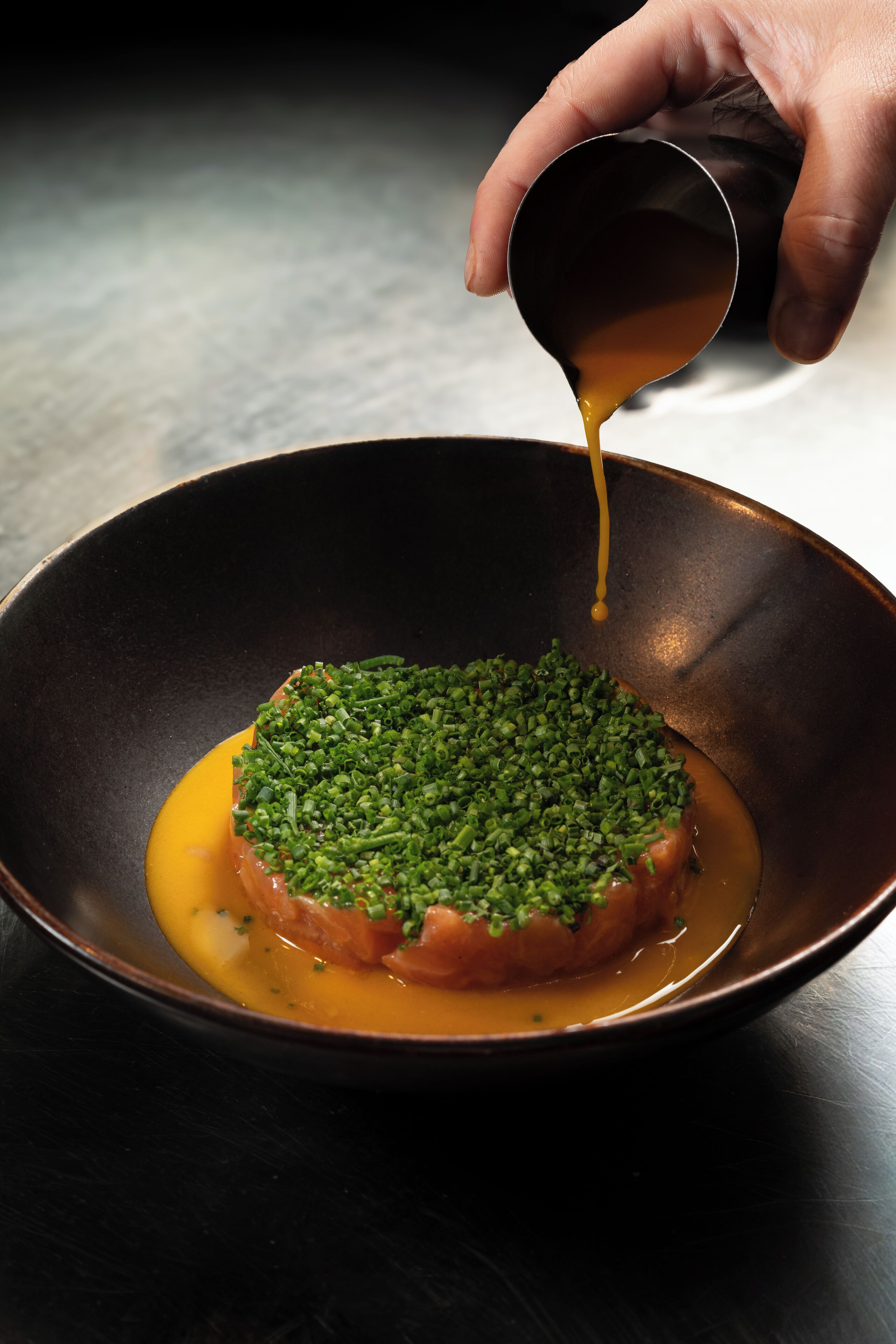A hand pouring sauce over a food item in a bowl.