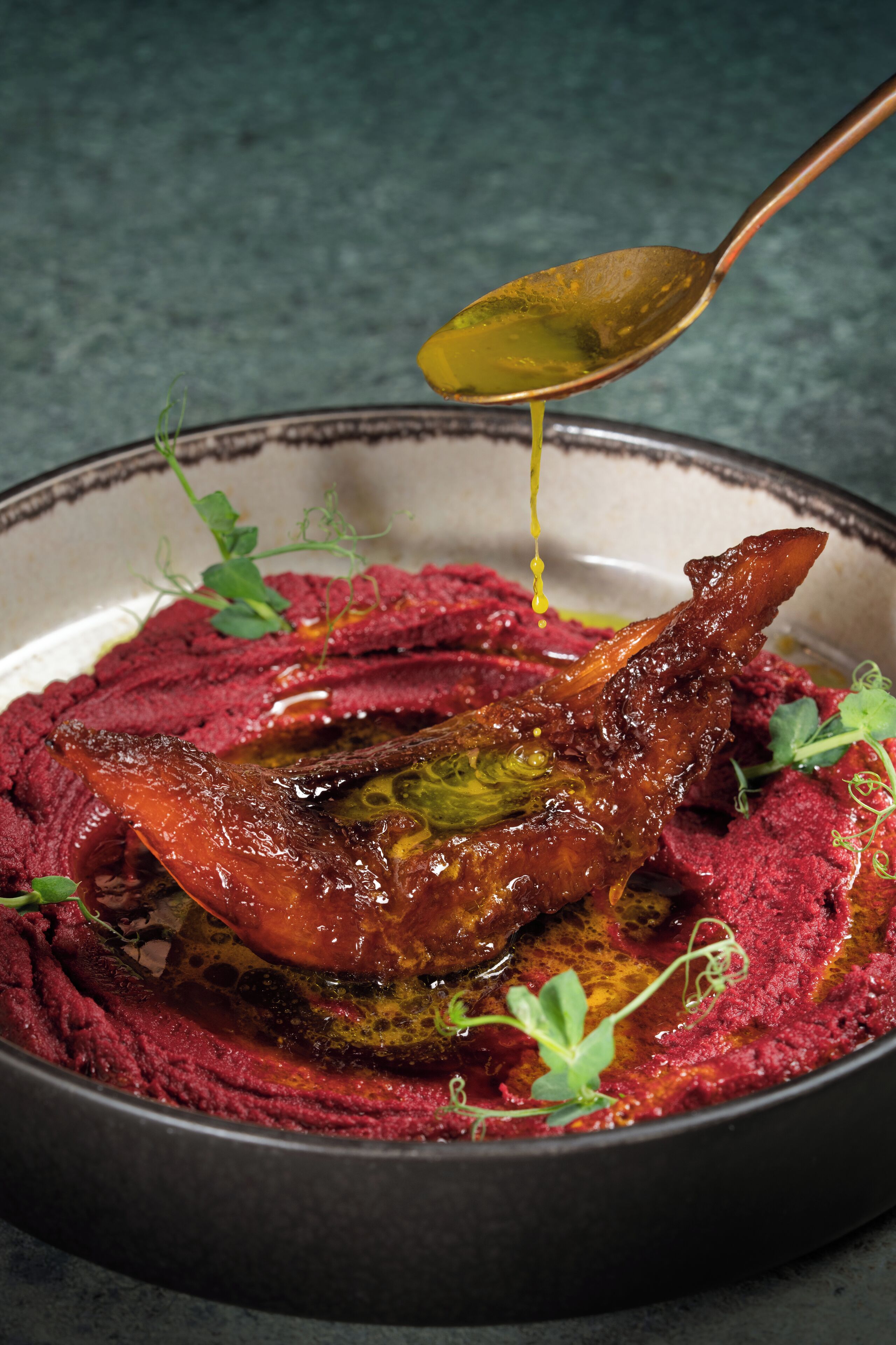 A dish with a roasted duck leg and a spoon pouring sauce over it.