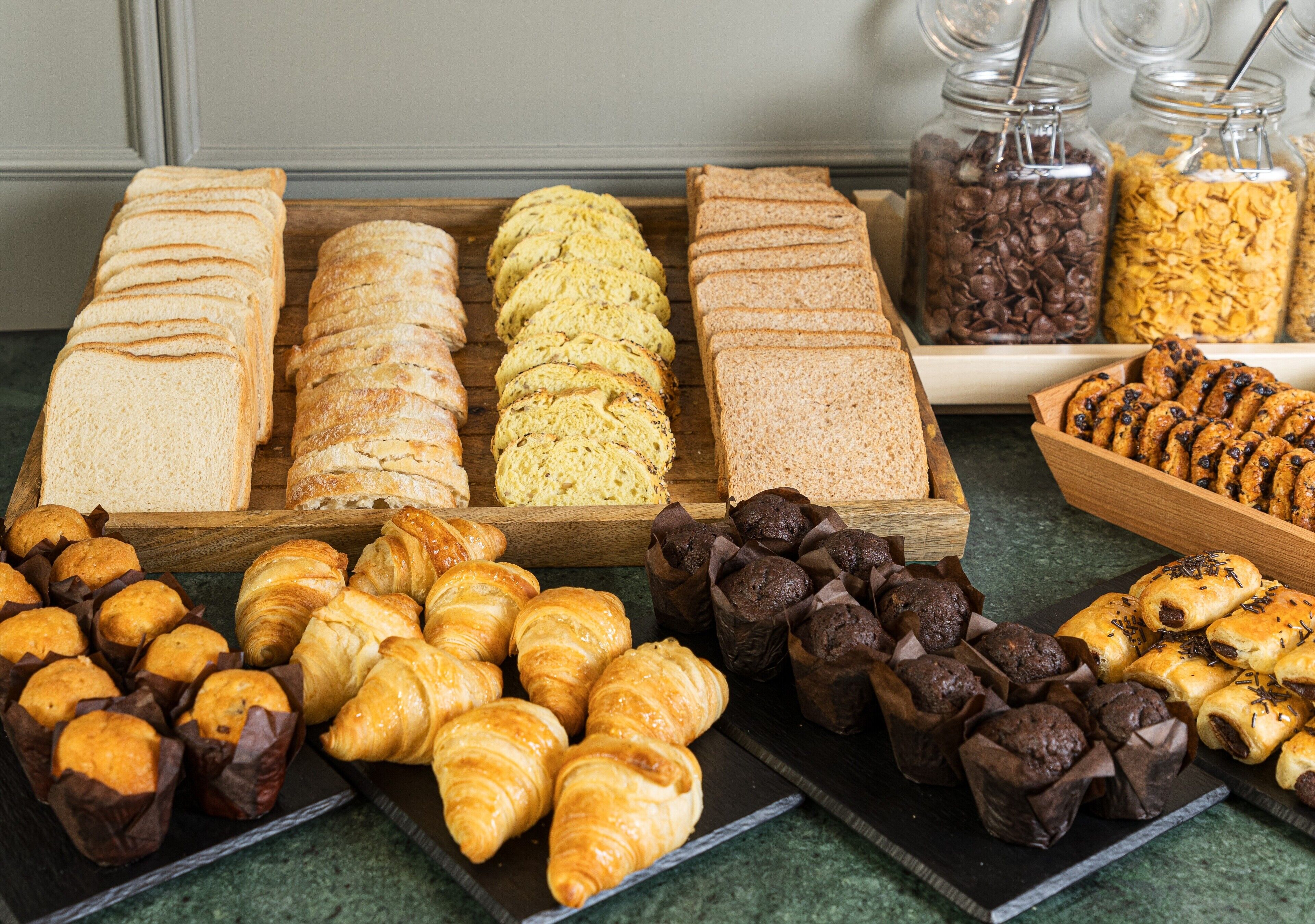 Variedad de productos horneados, como pan, croissants, muffins y pasteles, expuestos en un mostrador.