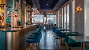 Un espace bar doté d’un long comptoir, de tabourets de bar verts et offrant une vue sur la ville grâce à de grandes fenêtres.