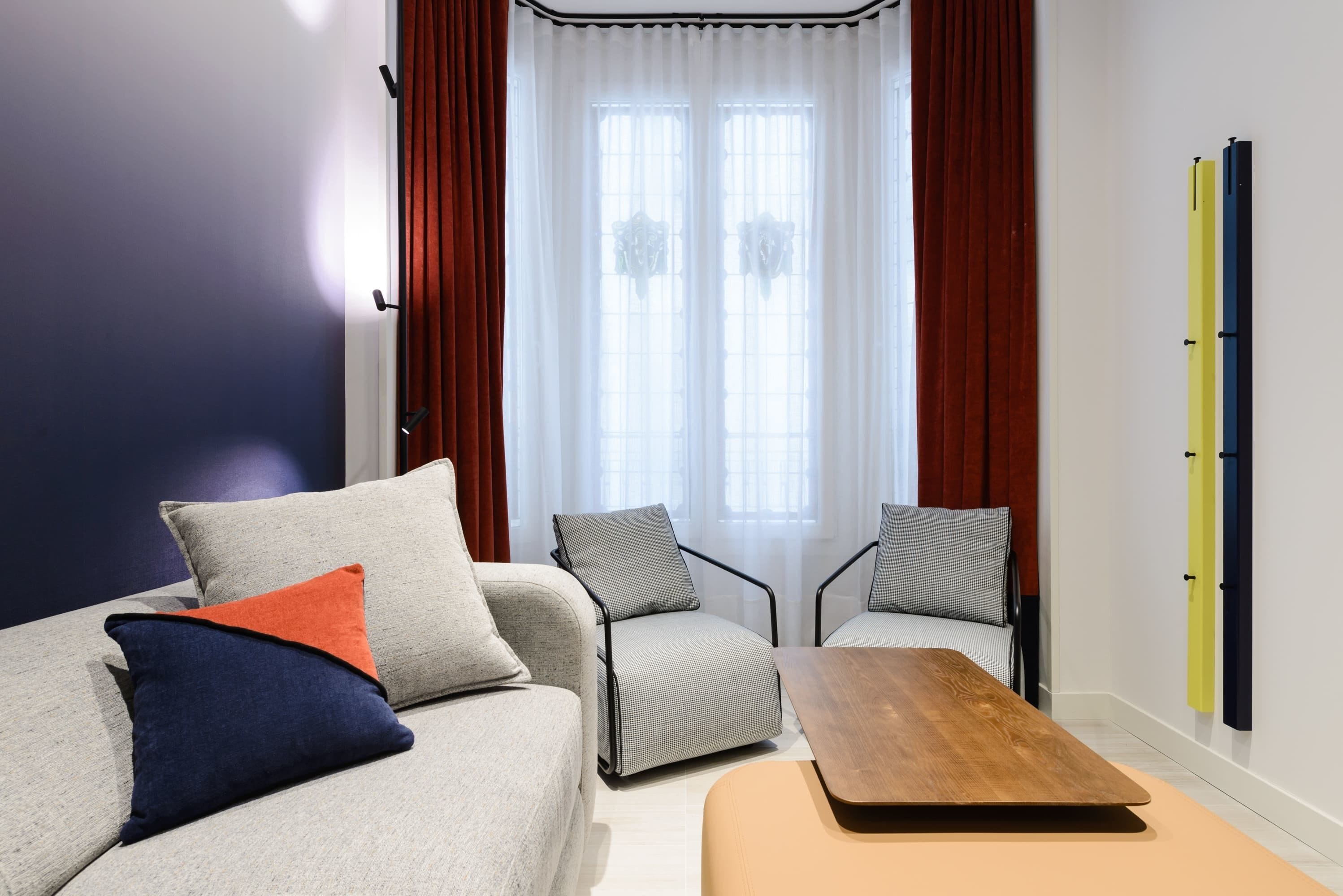 Una sala moderna con un sofá, dos sillones, una mesa de centro de madera y un ventanal con cortinas.