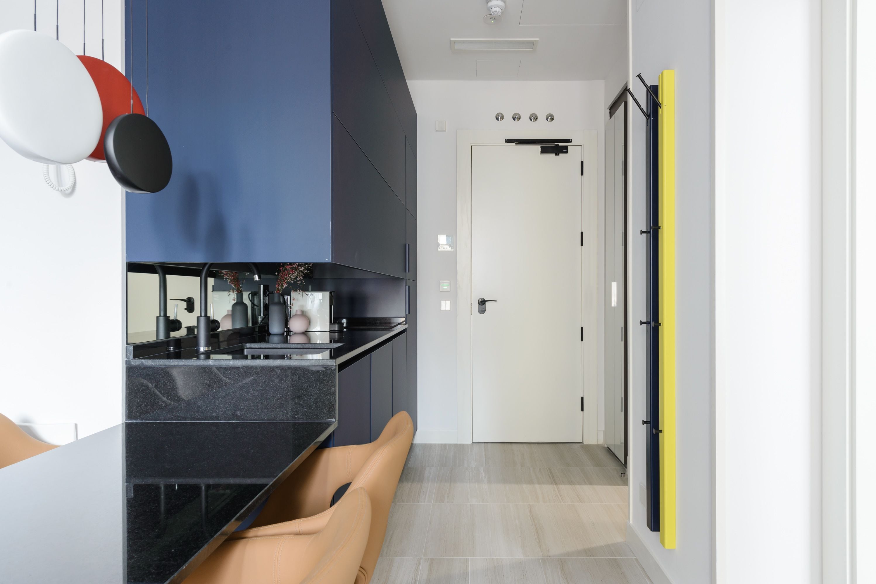 Une cuisine moderne avec un plan de travail noir, une chaise beige et une porte blanche en arrière-plan.
