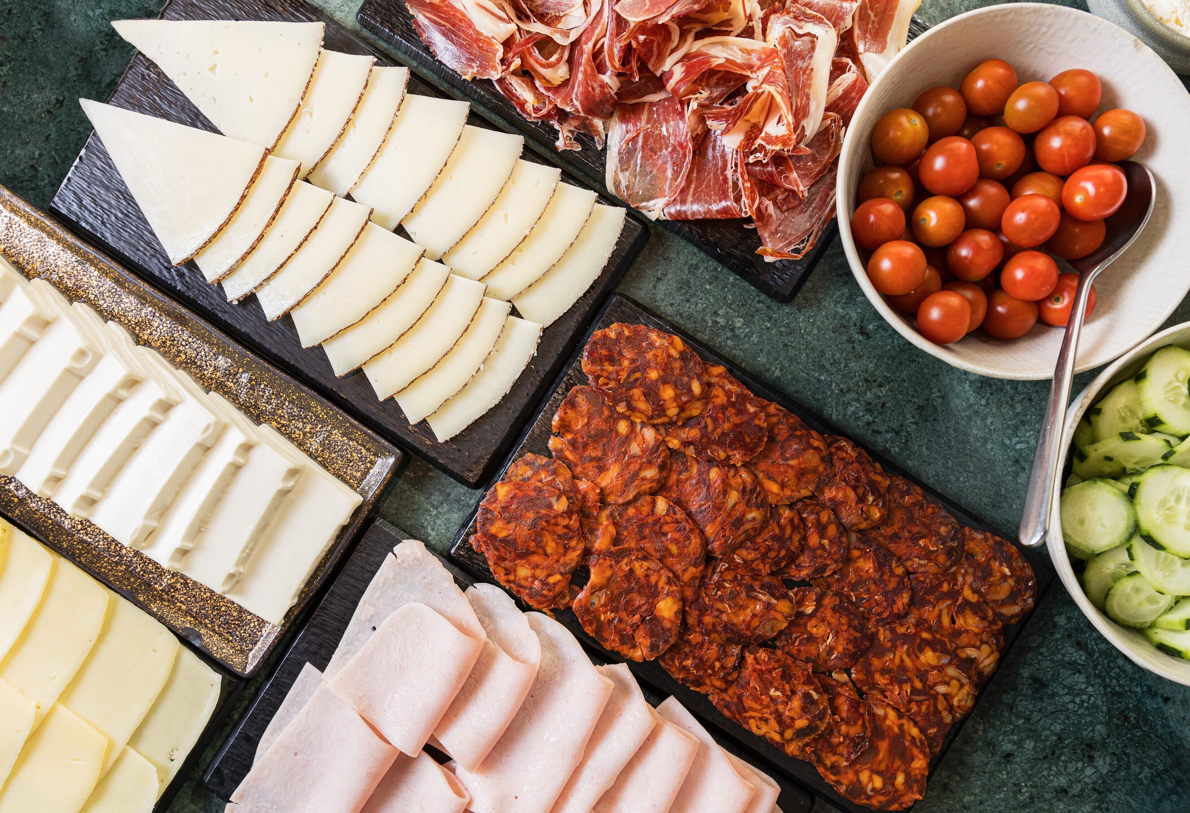 A variety of cheeses, cured meats, and tomatoes on a table.