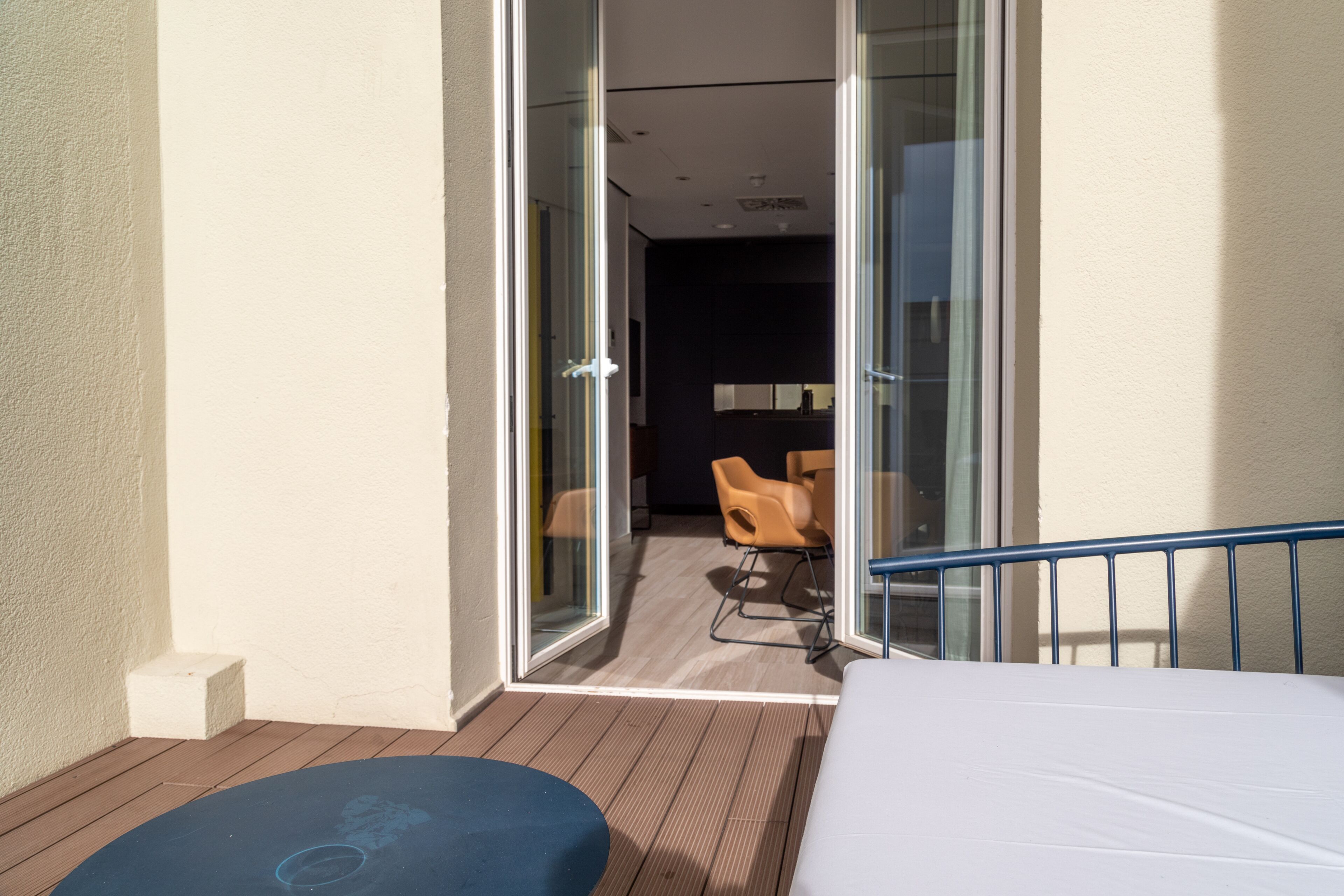 Un balcone con un letto, una sedia e una porta vetrata che dà su un ambiente interno con una sedia e un tavolo.
