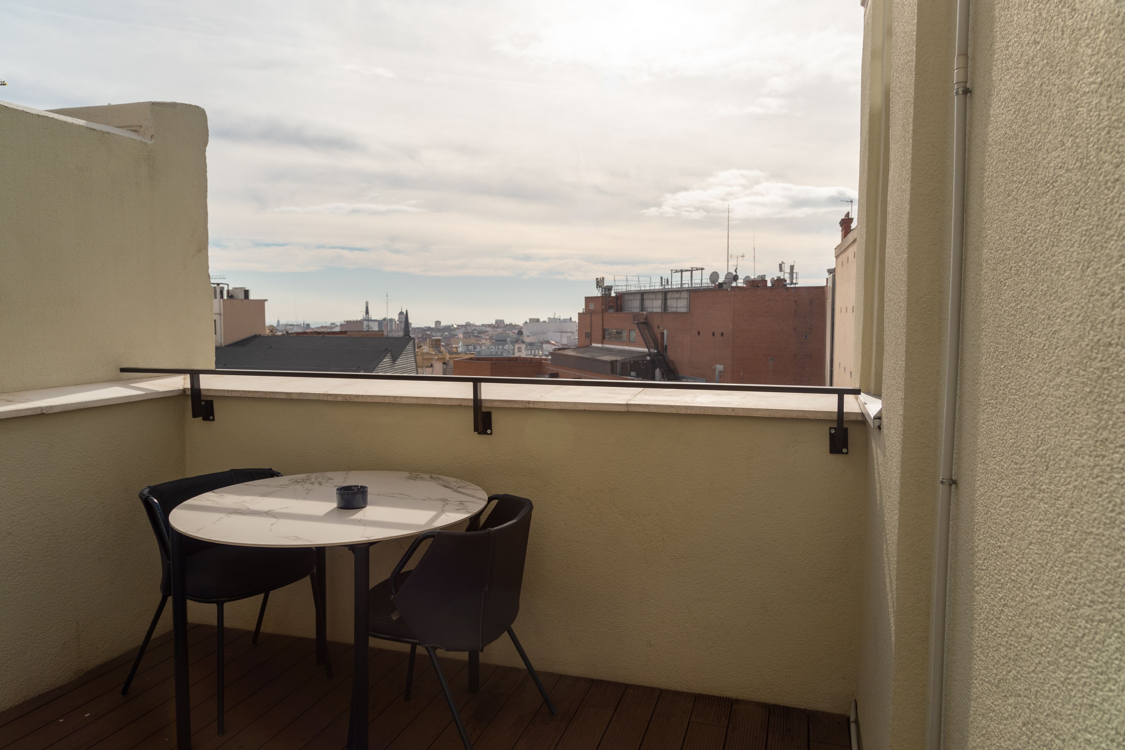 A balcony with a round table and two chairs, overlooking a cityscape.