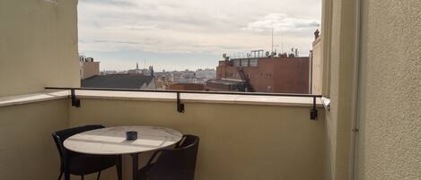 A balcony with a round table and two chairs, overlooking a cityscape.