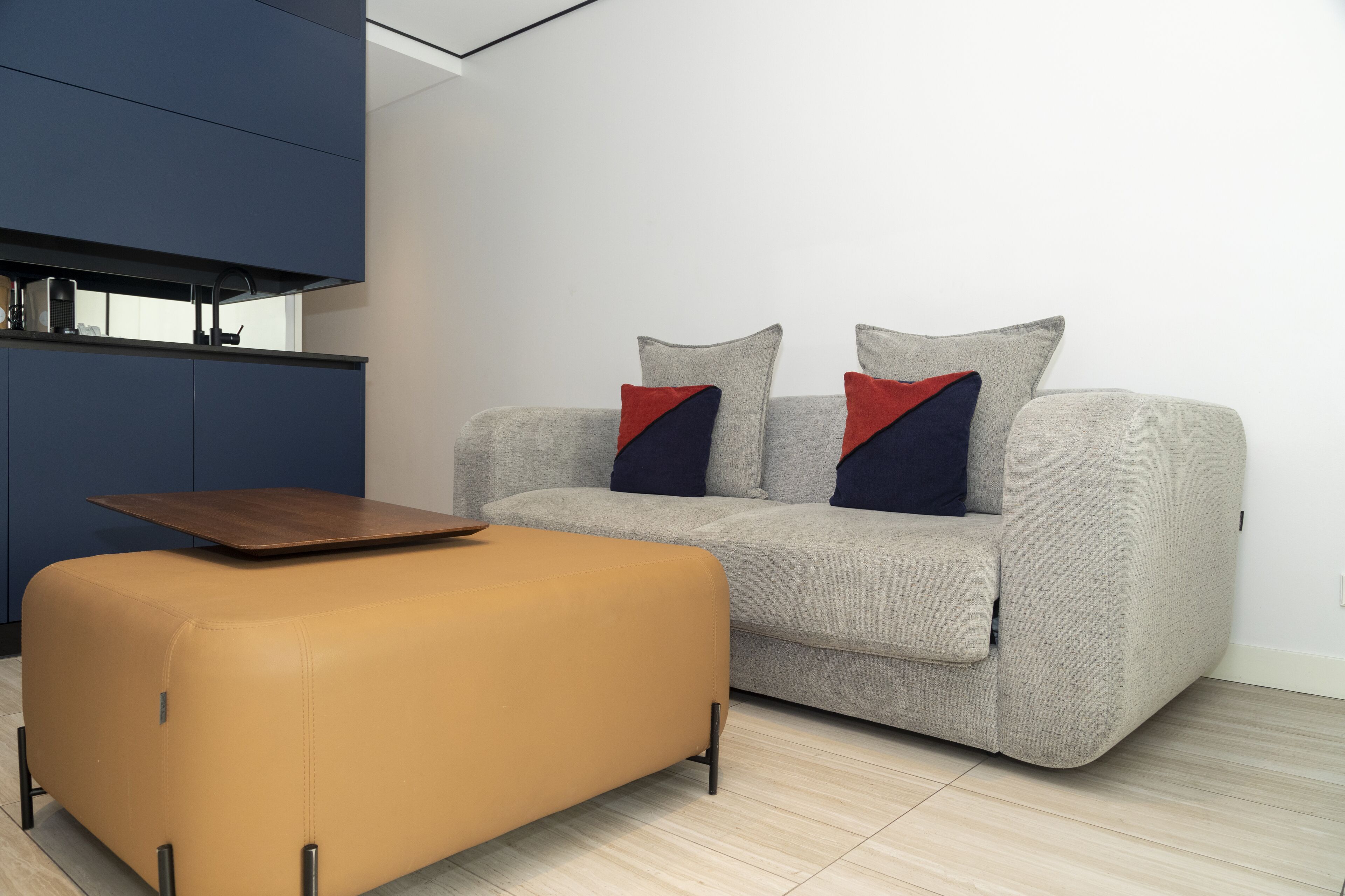 Uma sala de estar moderna com um sofá cinzento, um banquinho amarelo mostarda e uma mesa de centro de madeira.