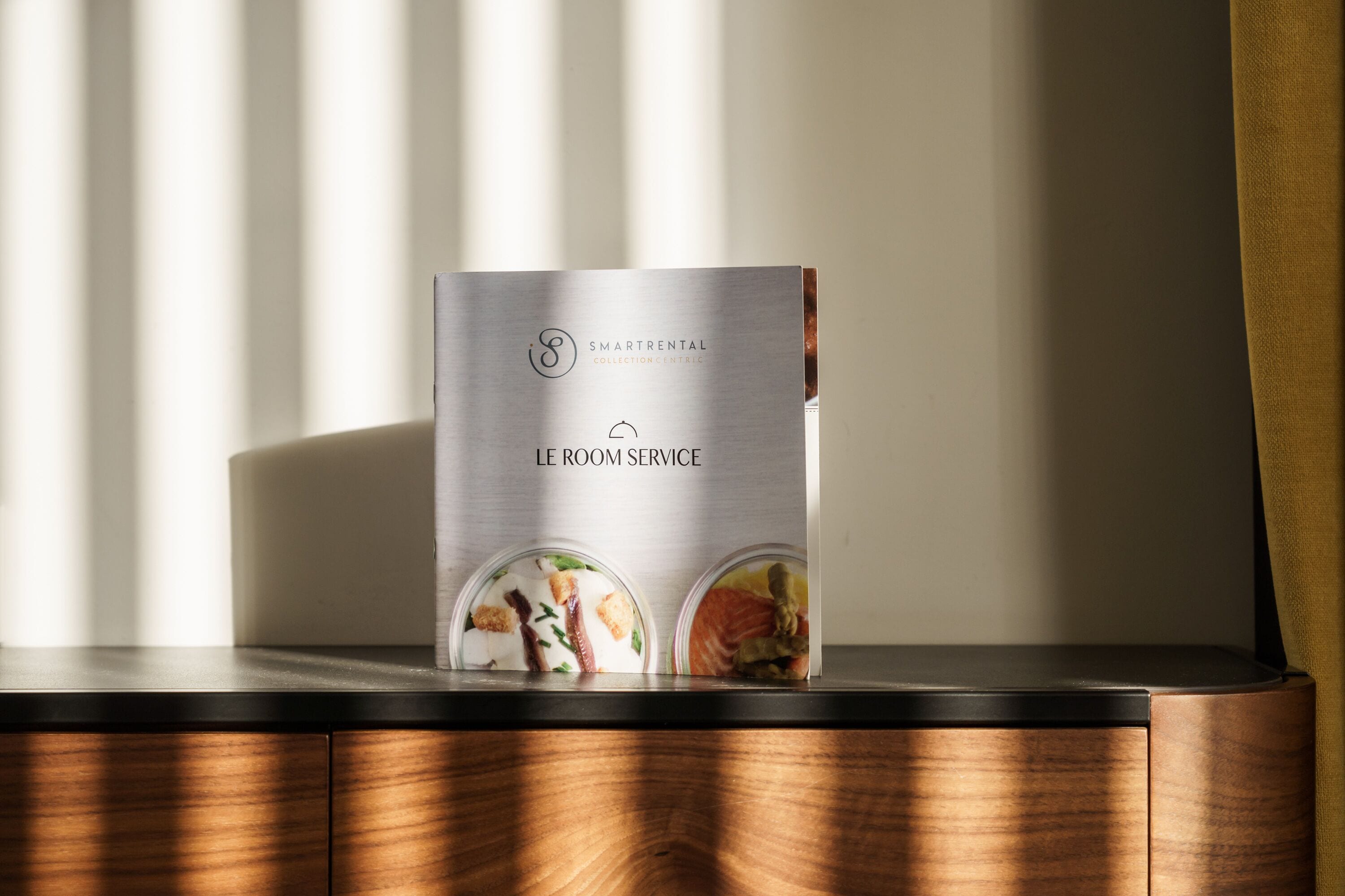 Een brochure met de titel 'SMARTRENTAL COLLECTION INTRELIC' op een houten oppervlak, met een raam op de achtergrond.