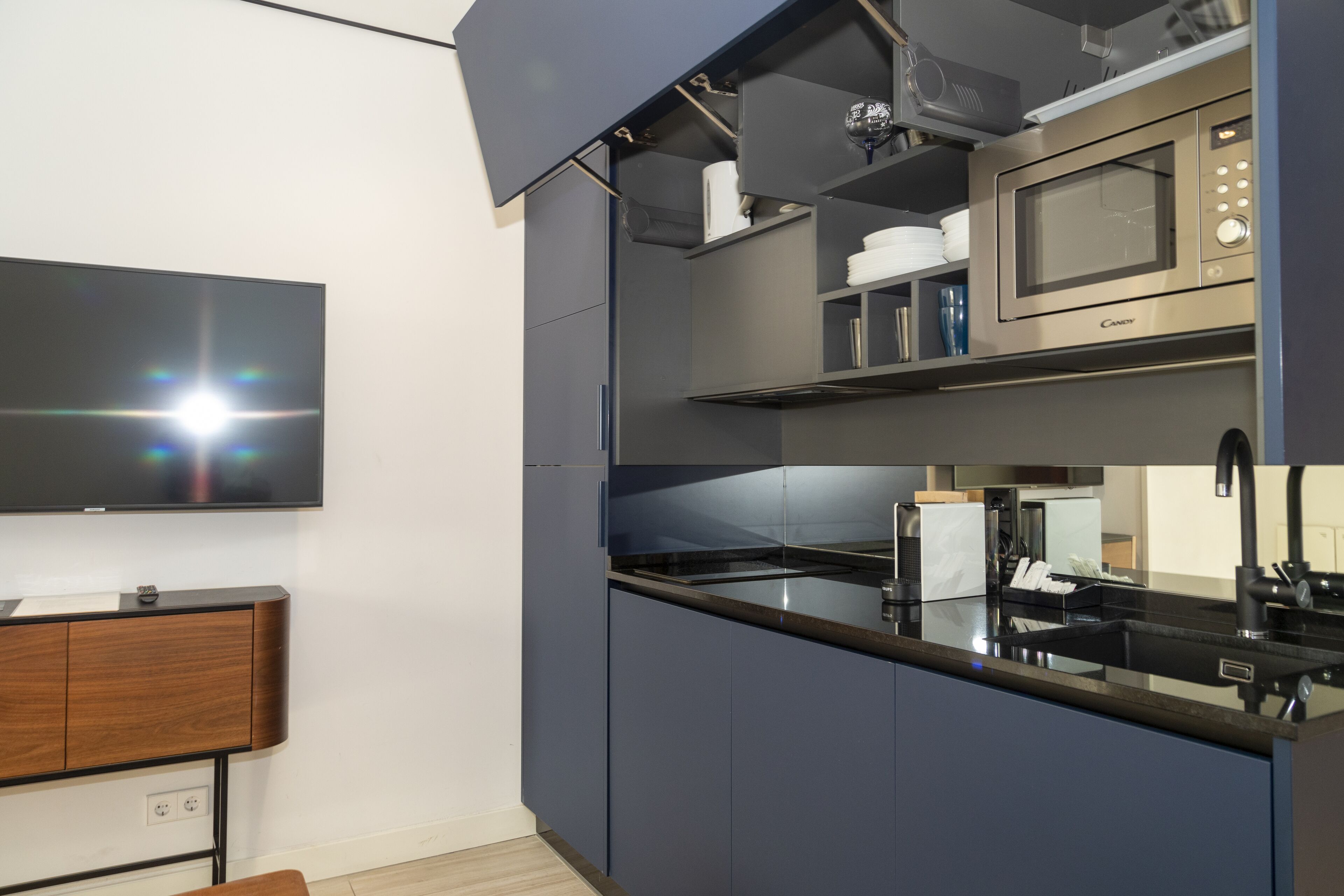 A modern kitchen with a flat-screen TV, built-in microwave, and dark cabinetry.