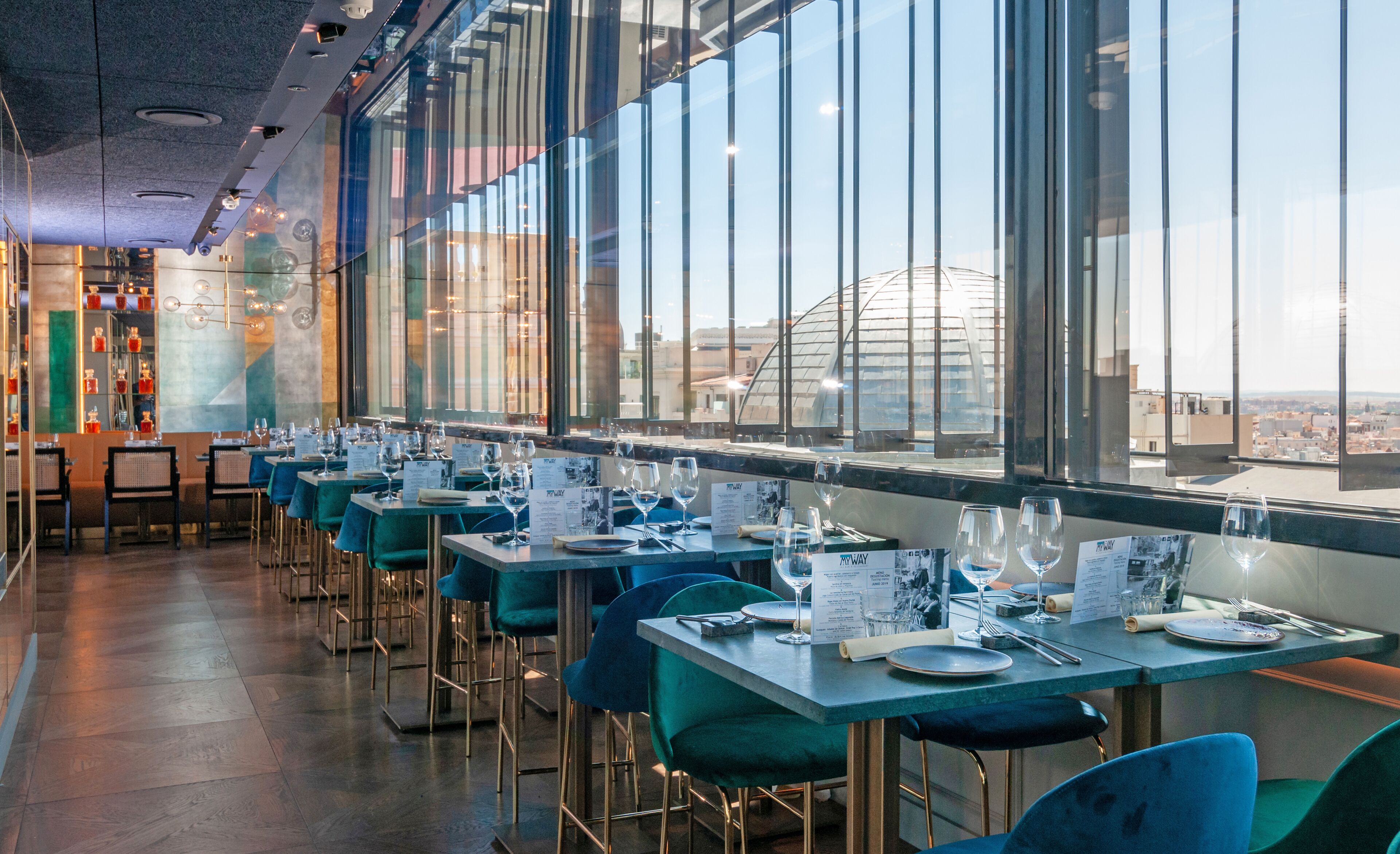 A restaurant with tables and chairs, menus, and a view of the city through large windows.