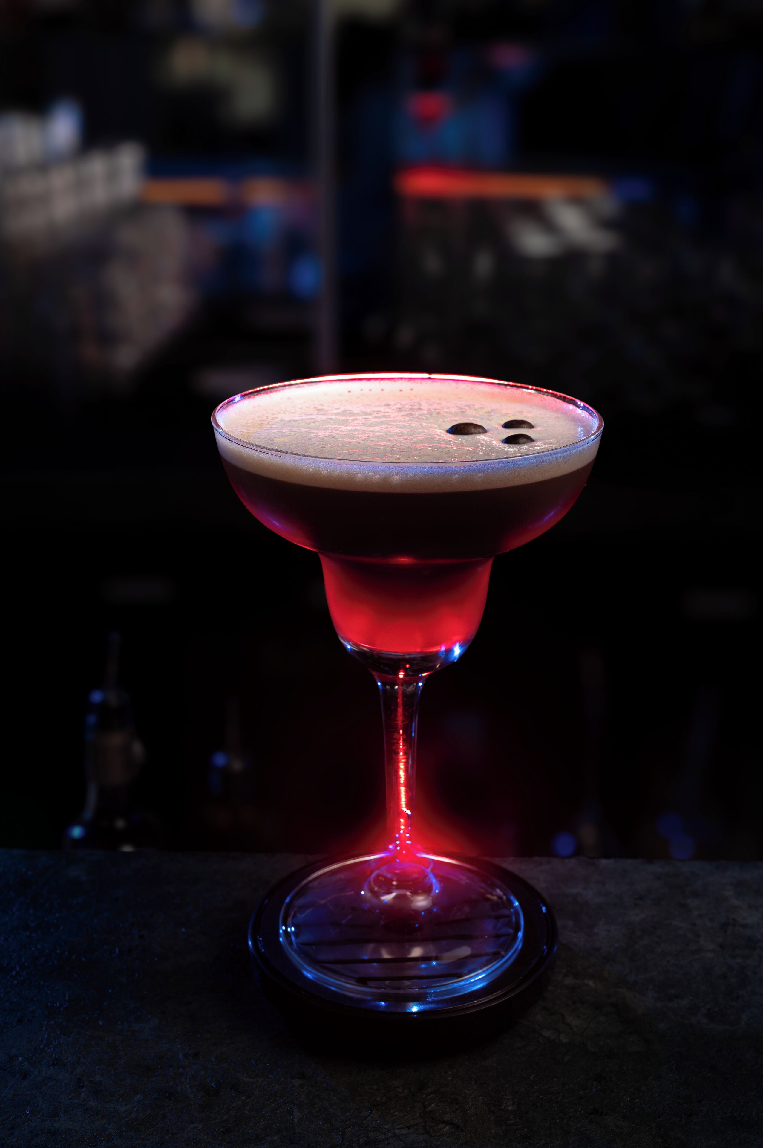 Un cocktail in un bicchiere da martini, con una schiuma in superficie, illuminato da una fonte di luce.