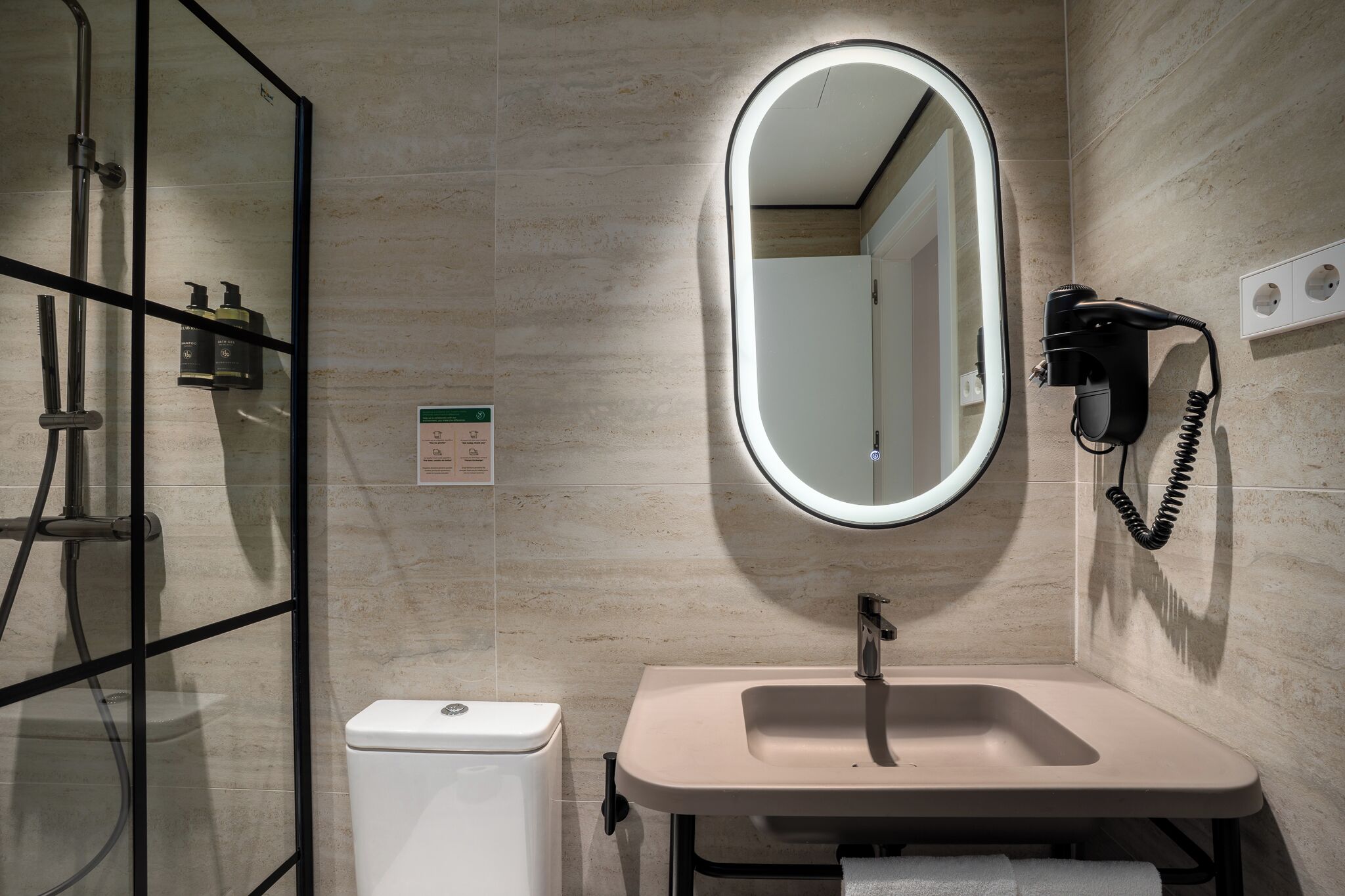 A bathroom with a glass-enclosed shower, a sink with a mirror, and a hairdryer mounted on the wall.