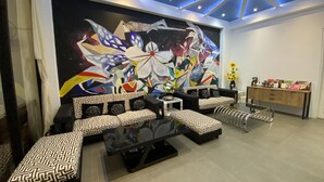 Un salon moderne agrémenté d’une grande fresque murale abstraite, d’un ensemble de canapés noir et blanc à motifs, d’une table basse en verre et d’un buffet en bois sur lequel sont disposés divers objets.