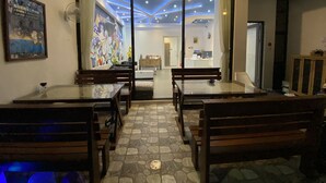 Un restaurant au décor moderne, avec un espace de restauration central agrémenté de bancs et de tables, une fresque colorée sur le mur du fond et un plafond illuminé par des jeux de lumière bleus.
