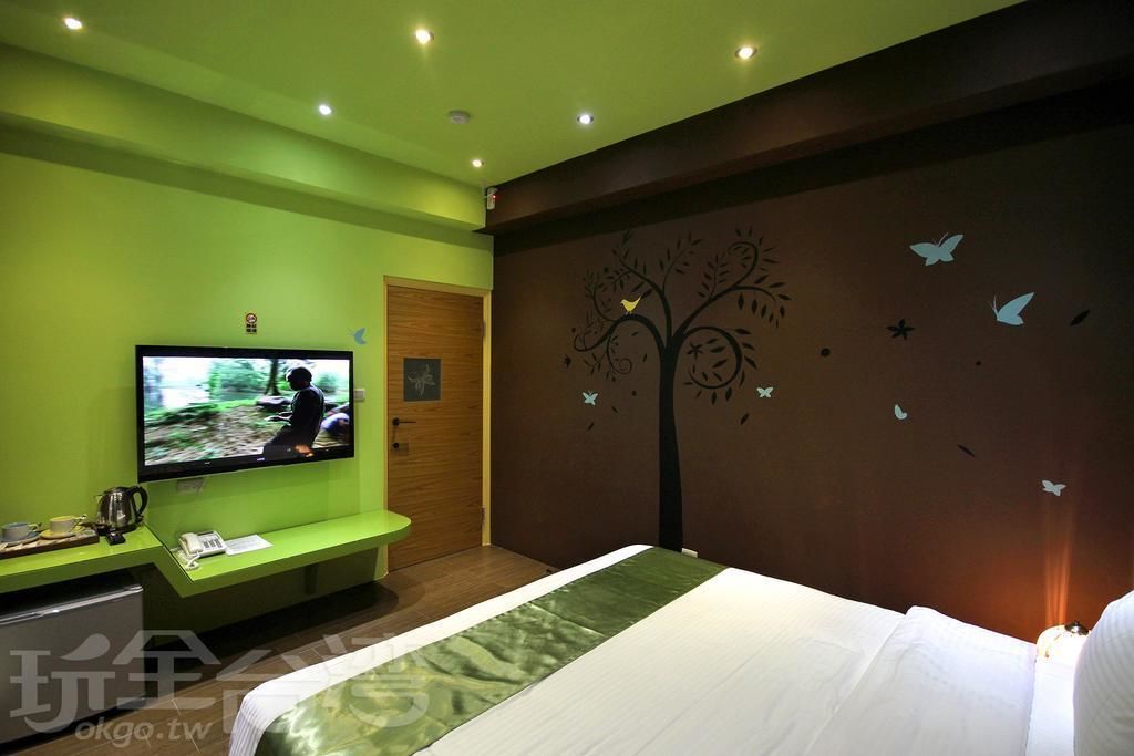 A hotel room with a bed, a television on a stand, a bench, and a wall with a tree and butterfly decal.