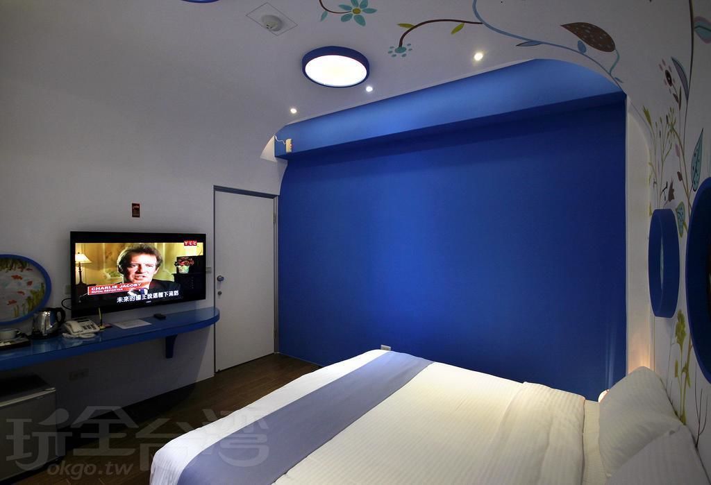Une chambre à coucher avec un lit, un téléviseur posé sur un meuble, et un mur d’accent bleu.