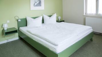 Una cama bien tendida con sábanas blancas en una habitación con paredes y cabecera verdes.