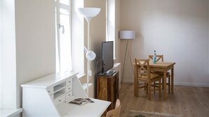 Une pièce avec un bureau blanc, une télévision, une lampe et une table à manger avec des chaises.