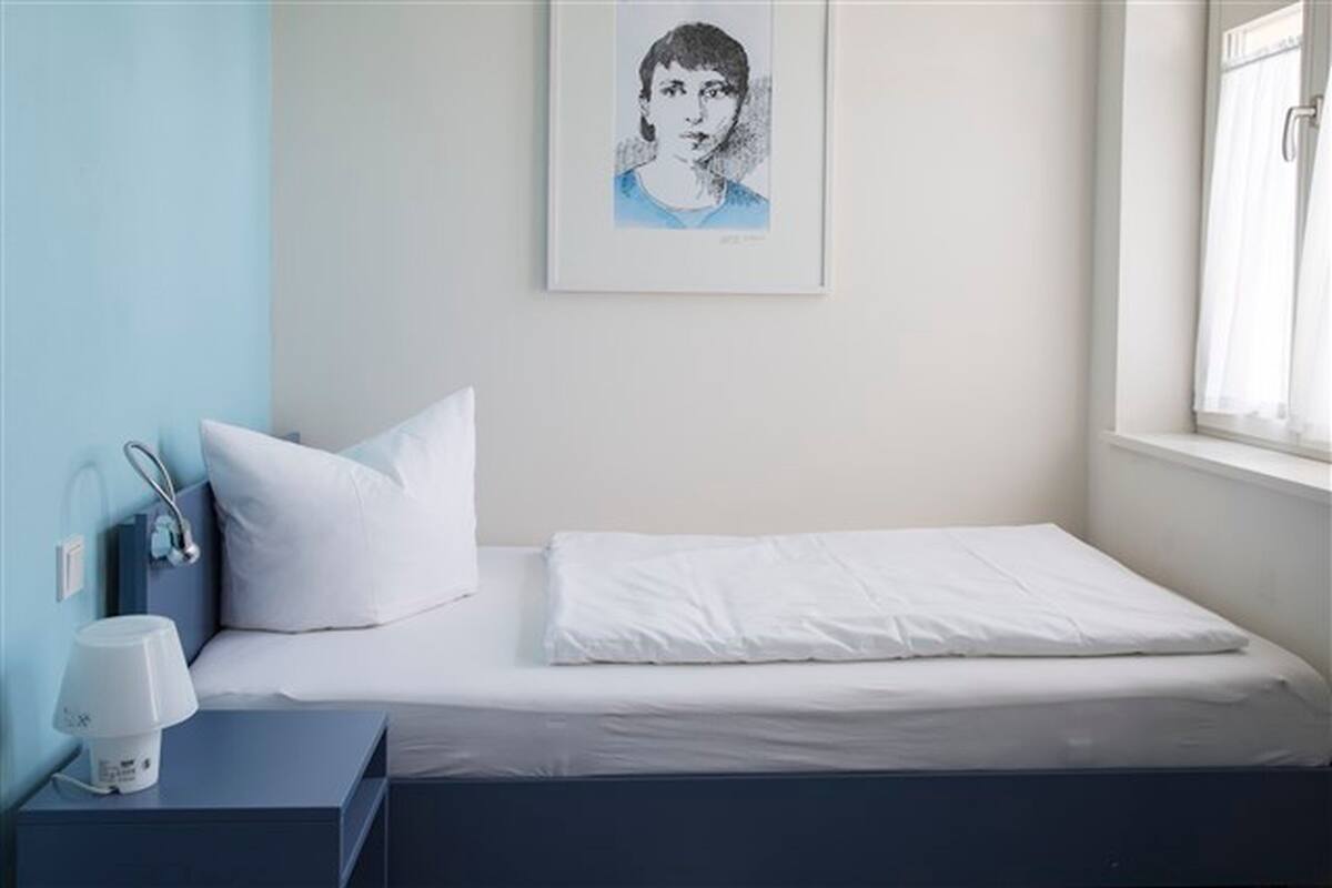 Un lit bien fait, avec une literie blanche, une table de chevet avec une lampe et un tableau encadré au mur.