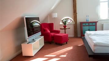 Habitación de hotel con televisión, una silla roja, reposapiés, una mesita con una planta y una cama.