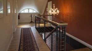 Un hall spacieux doté d’un plancher en bois, d’un tapis décoratif, d’un escalier avec une rampe en métal et d’un lustre.