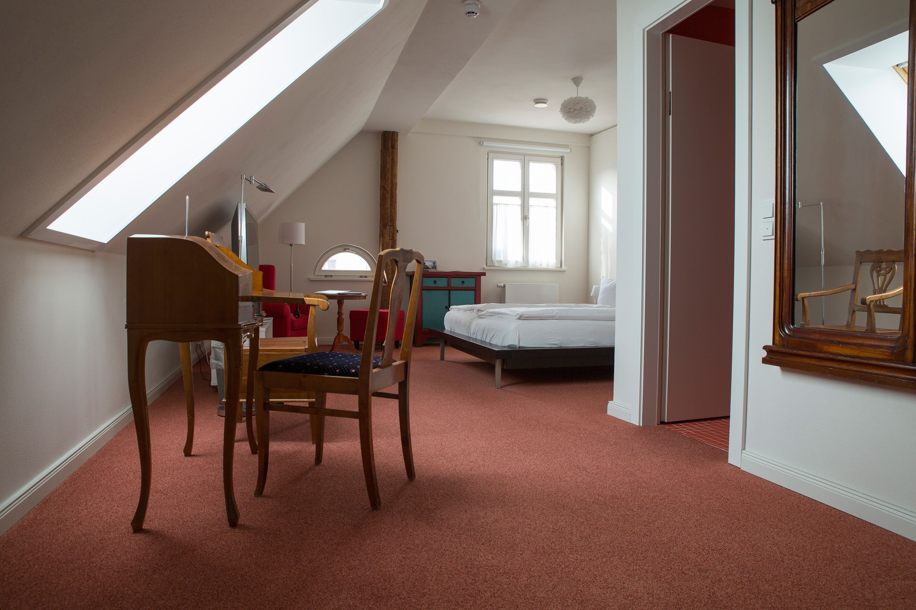 Une chambre avec un plafond en pente, un lit, une chaise, un bureau et une fenêtre.
